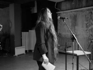 A woman performing on stage with a microphone in a black and white setting.