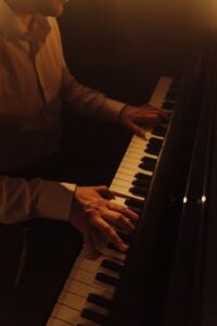 Close-up of a man playing piano, emphasizing hands and keys with warm lighting.